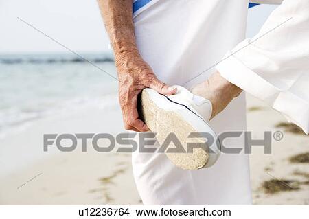 Close up of a senior man putting on his shoes on a beach View Large Photo Image Picture - Close up of a senior man putting on his shoes on a beach. Fotosearch