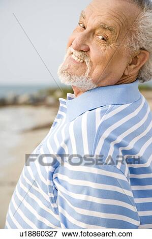 Portrait of a senior man standing on a beach smiling View Large Photo Image Stock Photo - Portrait of a senior man standing on a beach smiling. Fotosearch
