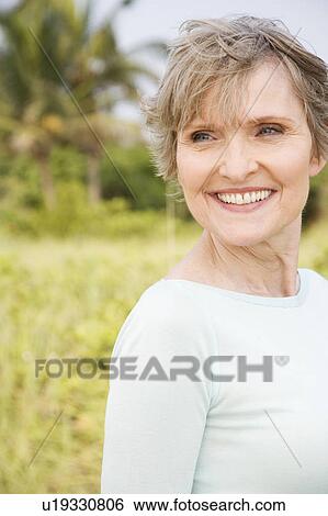 Stock Photograph - Portrait of a smiling senior woman in a tropical dune setting . Fotosearch