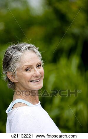 Stock Image - Portrait of a smiling senior woman in front of tropical foliage . Fotosearch