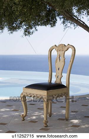 Stock Photography - A chair under a tree by a swimming pool. Fotosearch