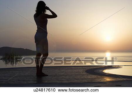 Stock Image - A woman taking a photograph of a sunset. Fotosearch