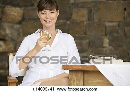 A woman drinking a glass of wine sitting at a table View Large Photo Image Stock Image - A woman drinking a glass of wine sitting at a table. Fotosearch