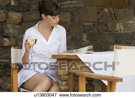Stock Photo - A woman drinking a glass of wine sitting at a table. Fotosearch