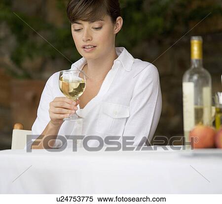 Stock Photography - A woman drinking a glass of wine sitting at a table. Fotosearch