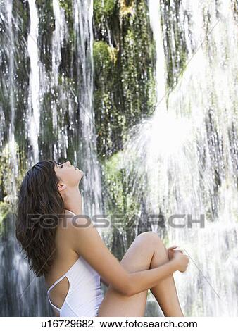 Stock Image - A woman sitting by a waterfall. Fotosearch