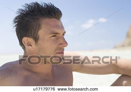 A man sitting on a beach View Large Photo Image Stock Photograph - A man sitting on a beach. Fotosearch