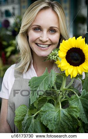 Woman florist standing at the entrance to her shop, holding a sunflower View Large Photo Image Stock Image - Woman florist standing at the entrance to her shop, holding a sunflower. Fotosearch
