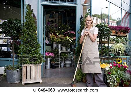 Woman florist standing at the entrance to her shop, leaning on a broom View Large Photo Image Stock Photo - Woman florist standing at the entrance to her shop, leaning on a broom. Fotosearch