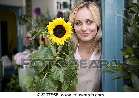 Woman florist standing at the entrance to her shop, holding a sunflower View Large Photo Image Stock Photo - Woman florist standing at the entrance to her shop, holding a sunflower. Fotosearch
