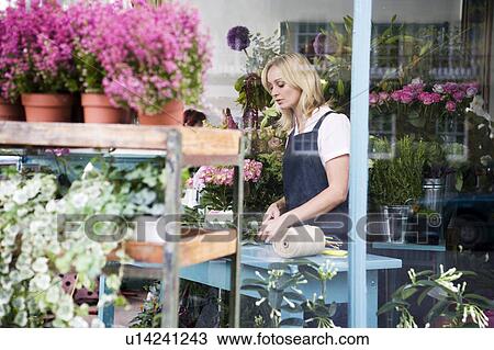 Stock Image - Woman florist viewed through the shop front. Fotosearch
