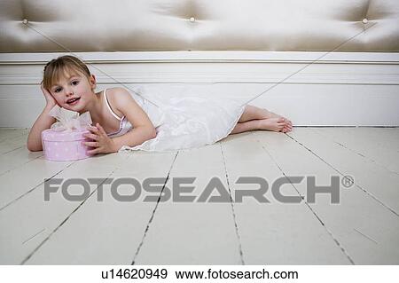Stock Photo - Little girl in a party dress, laying on the floor with a present. Fotosearch
