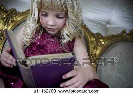 Stock Image - Little girl in a party dress, reading a book. Fotosearch