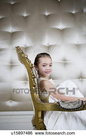 Stock Photograph - Little girl sitting in an ornate chair wearing a party dress. Fotosearch