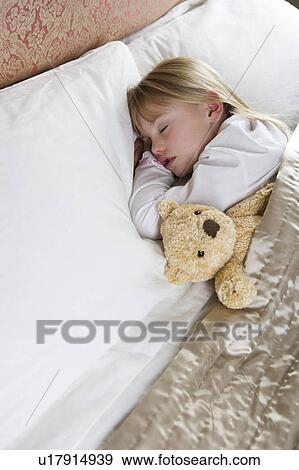 Stock Photo - Young girl asleep in her bed with a teddy bear . Fotosearch