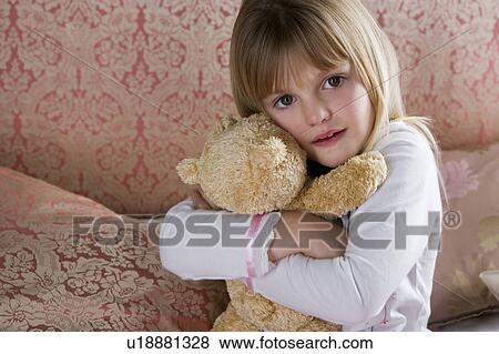 Stock Photo - Young girl in her bedroom hugging a teddy bear . Fotosearch