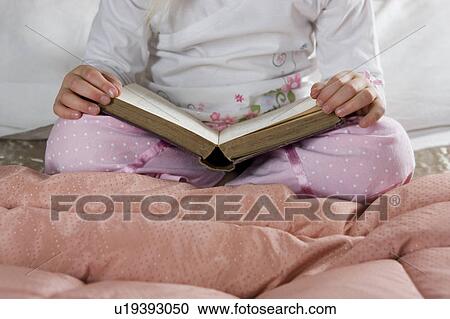Stock Image - Young girl in her bedroom reading a book . Fotosearch