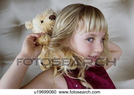 Stock Image - Young girl in party dress, holding a teddy bear. Fotosearch