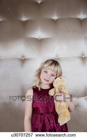 Stock Photo - Young girl in party dress, holding a teddy bear. Fotosearch