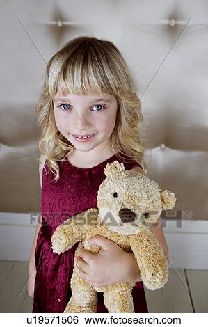 Stock Photograph - Young girl in party dress, holding a teddy bear. Fotosearch