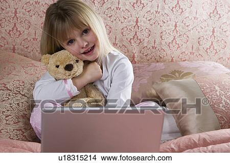 Young girl using a laptop computer in her bedroom and holding a teddy bear View Large Photo Image Picture - Young girl using a laptop computer in her bedroom and holding a teddy bear. Fotosearch