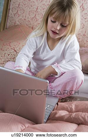 Stock Image - Young girl using a laptop computer in her bedroom . Fotosearch