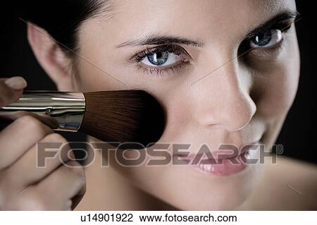 Stock Image - Woman applying blusher or bronzer on her face. Fotosearch