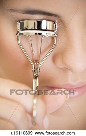 Stock Photo - Woman curling her eyelashes. Fotosearch