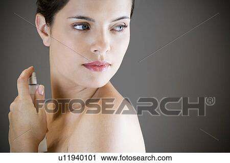 Stock Image - Young woman spraying perfume on her neck. Fotosearch