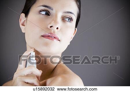 Stock Image - Young woman spraying perfume on her neck. Fotosearch