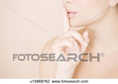 Stock Image - Close-up of woman holding a finger to her lips, speak no evil. Fotosearch
