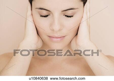 Stock Photo - Portrait of young woman holding her hands beside her face, eyes closed. Fotosearch