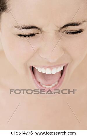 Stock Photograph - Portrait of young woman with mouth open wide and eyes closed, screaming. Fotosearch