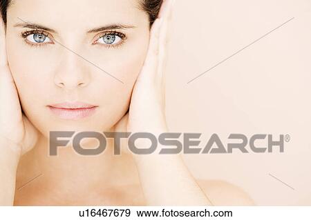 Stock Photo - Portrait of young woman's face with hands over her ears, hear no evil. Fotosearch