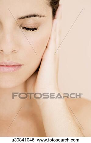 Stock Photograph - Portrait of young woman holding her hand beside her face, eye closed. Fotosearch