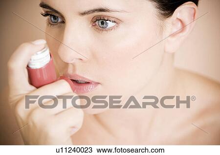 Stock Image - Female asthma sufferer using an inhaler. Fotosearch