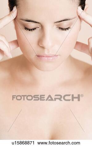 Stock Image - Portrait of young woman with eyes closed and fingers on her temples, concentrating. Fotosearch