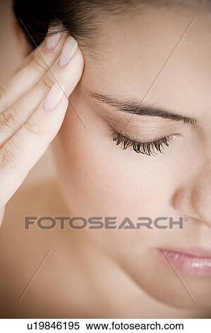 Stock Photography - Portrait of young woman with eyes closed and fingers on her temple, concentrating. Fotosearch