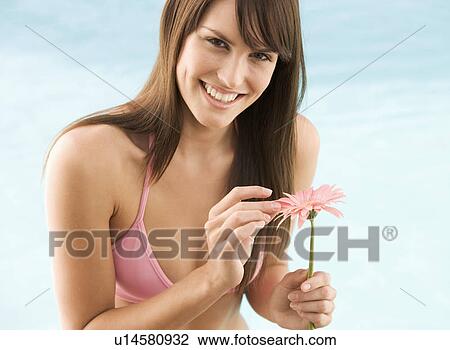 Stock Image - A young woman in a bikini holding a flower. Fotosearch
