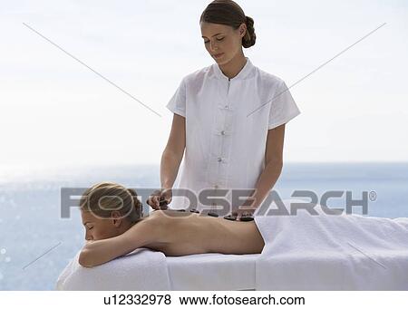 Stock Photo - A young woman receiving a hot stone holistic treatment. Fotosearch