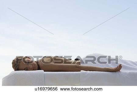 Stock Photograph - A young woman receiving a hot stone holistic treatment. Fotosearch