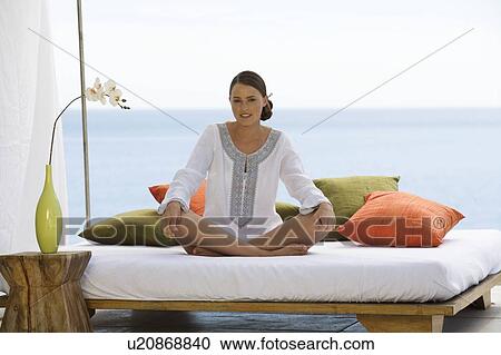 Stock Image - A young woman sitting on a bed. Fotosearch