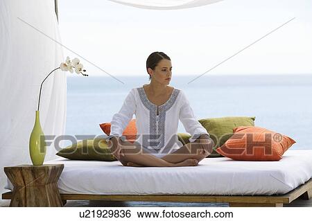 A young woman sitting on a bed View Large Photo Image Stock Photograph - A young woman sitting on a bed. Fotosearch