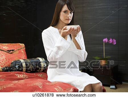 A woman drinking from a bowl sitting on a bed View Large Photo Image Stock Photo - A woman drinking from a bowl sitting on a bed. Fotosearch