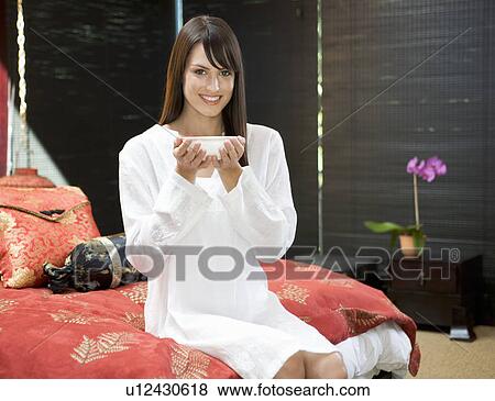 A woman drinking from a bowl sitting on a bed View Large Photo Image Stock Photo - A woman drinking from a bowl sitting on a bed. Fotosearch