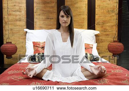 Stock Image - A woman sitting on a bed meditating. Fotosearch