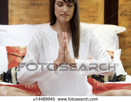 Stock Photography - A woman sitting on a bed meditating. Fotosearch