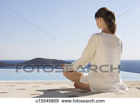 Stock Photo - A woman meditating by a pool. Fotosearch