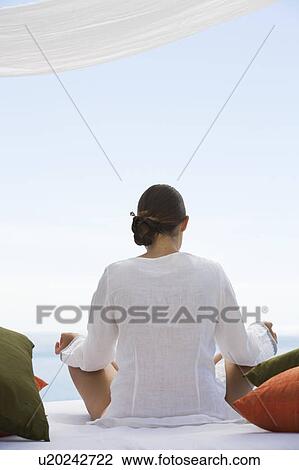 Stock Image - A young woman sitting on a bed. Fotosearch