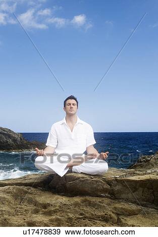 Stock Photo - A man meditating by the sea. Fotosearch